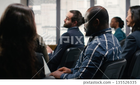 Business conference event with stage presentation and pitch by speaker. Mixed age audience and colleagues attend professional meeting with discussion and leadership training in auditorium. 135526335