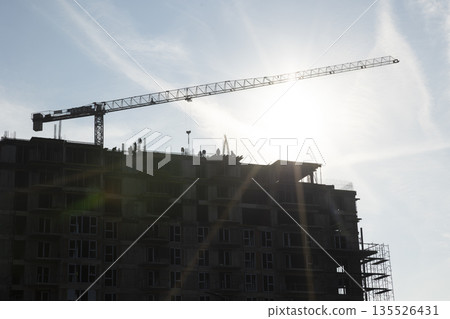 Crane operator installing metal components on high rise concrete condominium. Builders on rooftop using heavy machinery to fasten structural parts, completing unfinished apartment Crane operator installing metal components on high rise concrete condominium. Builders on rooftop using heavy machinery to fasten structural parts, completing unfinished apartment 135526431