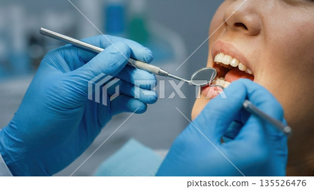 dentist works on a client's teeth in a modern dental office. The dentist uses tools while the client sits in the chair with their mouth open. The atmosphere is focused on care and treatment. dentist works on a client's teeth in a modern dental office. The dentist uses tools while the client sits in the chair with their mouth open. The atmosphere is focused on care and treatment. 135526476
