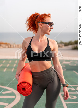 Fit redhead woman in sportswear holding rolled Fit redhead woman in sportswear holding rolled 135526968