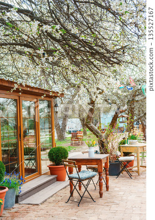 Spring outdoor garden table with bouquet of flowers under blooming trees in cozy backyard cafe Spring outdoor garden table with bouquet of flowers under blooming trees in cozy backyard cafe 135527167