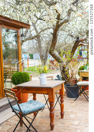 Spring outdoor garden table with bouquet of flowers under blooming trees in cozy backyard cafe Spring outdoor garden table with bouquet of flowers under blooming trees in cozy backyard cafe 135527168