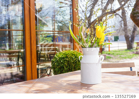 Spring bouquet of yellow tulips and white flowers in rustic metal vase on wooden table outdoors 135527169