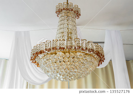 Luxury crystal chandelier hanging in elegant classic interior with white curtains Luxury crystal chandelier hanging in elegant classic interior with white curtains 135527176