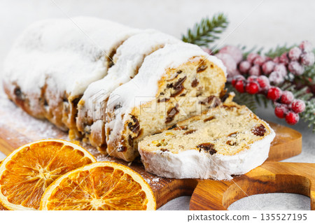 Traditional sliced Christmas stollen loaf with raisins and powdered sugar on wooden cutting board 135527195