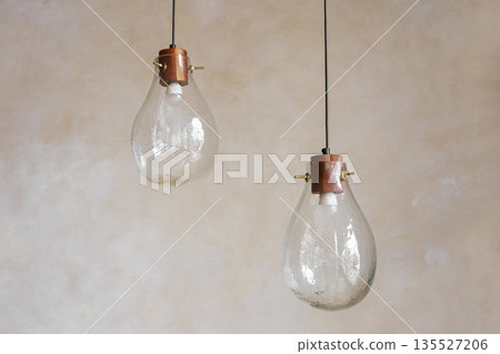Handmade glass pendant lights hanging in minimalist interior space on painted wall background Handmade glass pendant lights hanging in minimalist interior space on painted wall background 135527206