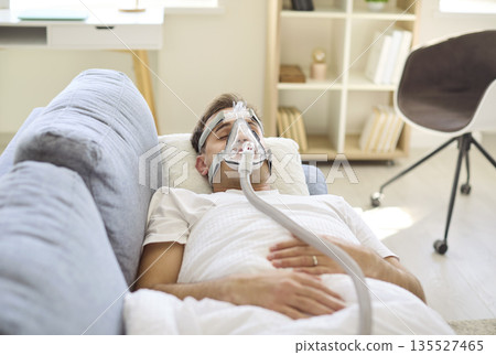 Man sleeping on couch with oxygen mask and CPAP hose for nighttime therapy Man sleeping on couch with oxygen mask and CPAP hose for nighttime therapy 135527465