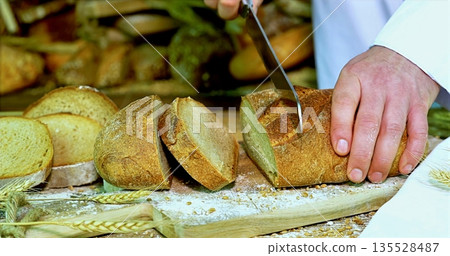 Bread Being Cut On Wooden Surface, Craftsman Slicing Crispy Bread With Knife On Textured Wooden Board 135528487