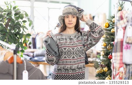 Young girl choosing winter hat in clothing store during Christmas Young girl choosing winter hat in clothing store during Christmas 135529313