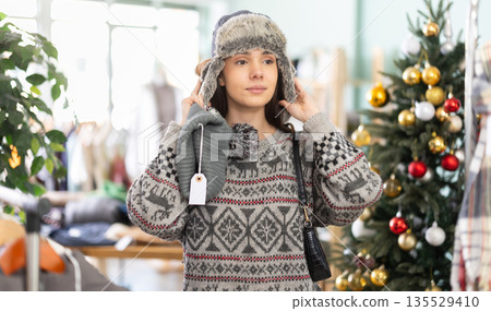 Girl spend time in shop, choose and try on winter hat. X mas shopping 135529410