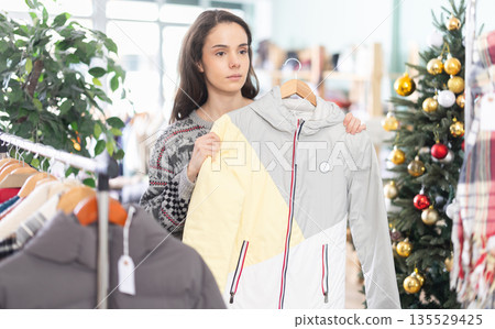 Young woman chooses down jacket in clothing store Young woman chooses down jacket in clothing store 135529425