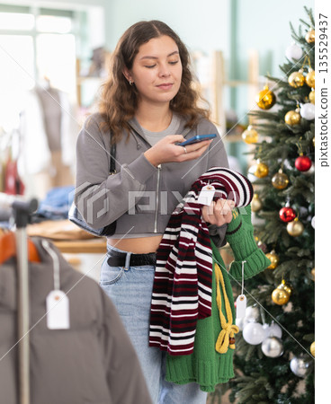 Young woman scanning qr code for sweater in store Young woman scanning qr code for sweater in store 135529437