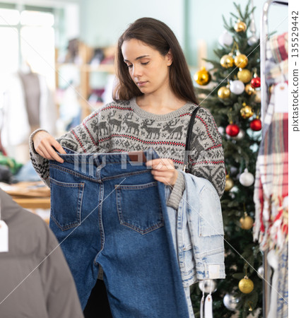 Young girl choosing jeans pantaloons in clothing store during Christmas 135529442