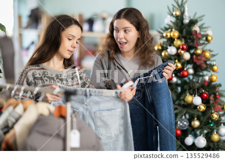 Two women carefully choose jeans against the background of a Christmas tree Two women carefully choose jeans against the background of a Christmas tree 135529486