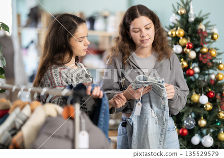 Two women carefully choose jeans against the background of a Christmas tree Two women carefully choose jeans against the background of a Christmas tree 135529579