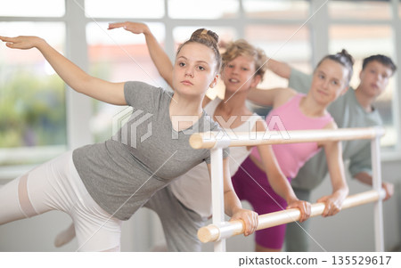 Teenagers ballet lovers learn to perform arabesque pose in choreography studio Teenagers ballet lovers learn to perform arabesque pose in choreography studio 135529617