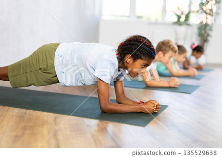 In sport studio with group of friends, African boy perform plank pose asana 135529638