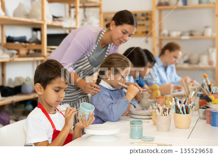 Attentive little boy painting handmade ceramic cup with brush 135529658
