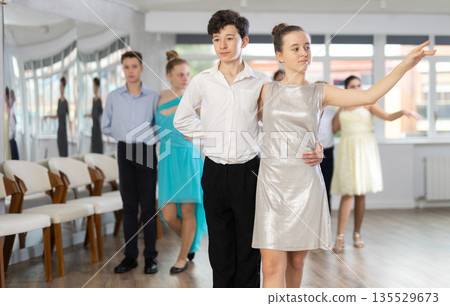 Positive teen boy and girl are dancing classic version of waltz in couple during lesson at studio 135529673