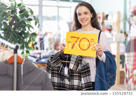Young woman holding sale sign in clothing store Young woman holding sale sign in clothing store 135529731