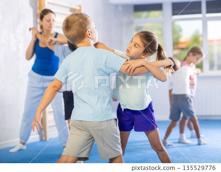 Children, boy and girl, working in pair mastering new self-defense moves at gym Children, boy and girl, working in pair mastering new self-defense moves at gym 135529776