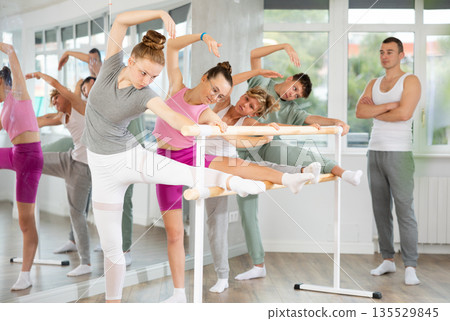 Ballet pose grand batman - girls and boys at a choreography lesson are learning ballet movements in studio Ballet pose grand batman - girls and boys at a choreography lesson are learning ballet movements in studio 135529845