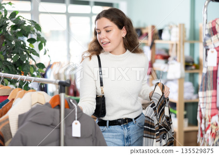 Woman holding a hanger with outerwear in her hands in a store 135529875