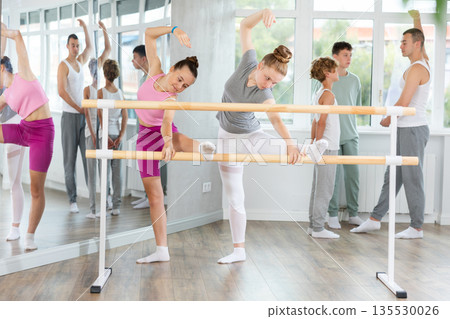 Two teenage girls practicing leg stretching exercise during ballet classes 135530026