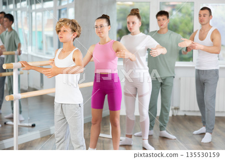 Teenage boys and girls practicing second position of ballet in dancehall 135530159