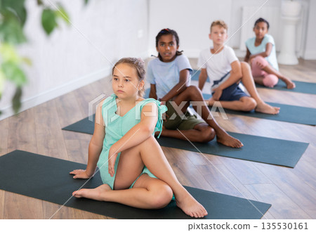 In sport studio with group of friends, girl perform Lord of Fishes asana, Ardha Matsyendrasana In sport studio with group of friends, girl perform Lord of Fishes asana, Ardha Matsyendrasana 135530161