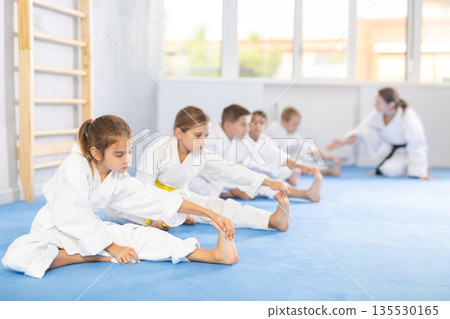 Children in white kimono doing stretching before karate ore judo training Children in white kimono doing stretching before karate ore judo training 135530165