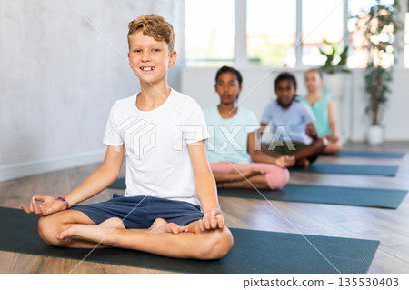 In sport studio with group of friends, boy perform lotus pose, Padmasana 135530403