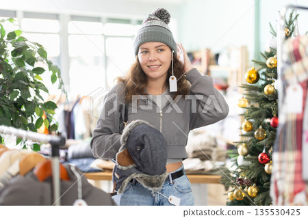 Girl spend time in shop, choose and try on winter hat. X mas shopping 135530425