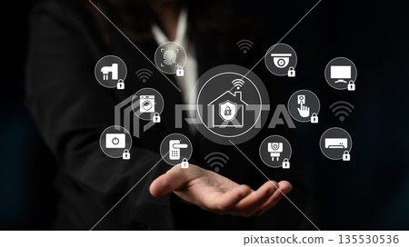 Woman in Business Suit Demonstrating Smart Home Technology with Various Connected Devices and Security Features in a Dark Background Gantry 135530536