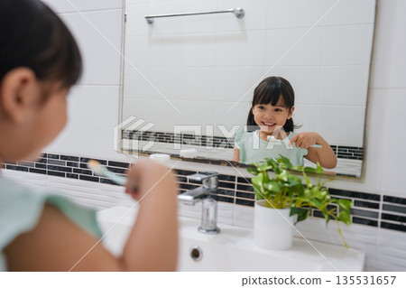 girl child brushing teeth at reflection in mirror in bathroom girl child brushing teeth at reflection in mirror in bathroom 135531657