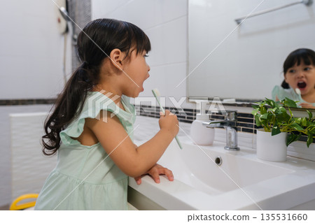 girl child brushing teeth at reflection in mirror in bathroom girl child brushing teeth at reflection in mirror in bathroom 135531660