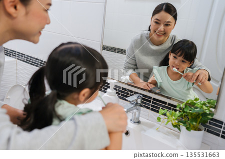 mother teaching girl child to brushing teeth at reflection in mirror in bathroom mother teaching girl child to brushing teeth at reflection in mirror in bathroom 135531663