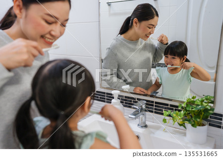 mother teaching girl child to brushing teeth at reflection in mirror in bathroom 135531665