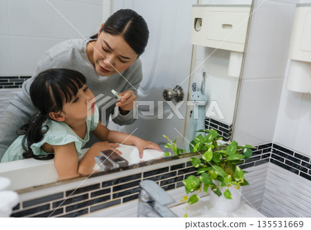 stubborn child girl refusing to brush her teeth in the bathroom. mother is trying to encourage her unhappy daughter during the morning routine, while child looks grumpy and resistant. stubborn child girl refusing to brush her teeth in the bathroom. mother is trying to encourage her unhappy daughter during the morning routine, while child looks grumpy and resistant. 135531669