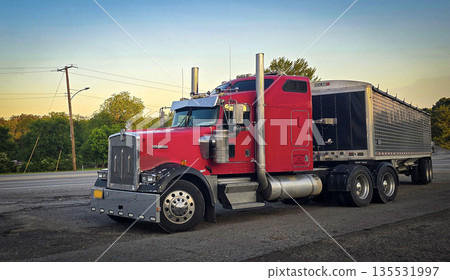 bold red semi truck with a long trailer sits in an open lot during sunset. The powerful rig highlights industrial design, chrome accents, and the rugged appeal of transportation and logistics bold red semi truck with a long trailer sits in an open lot during sunset. The powerful rig highlights industrial design, chrome accents, and the rugged appeal of transportation and logistics 135531997