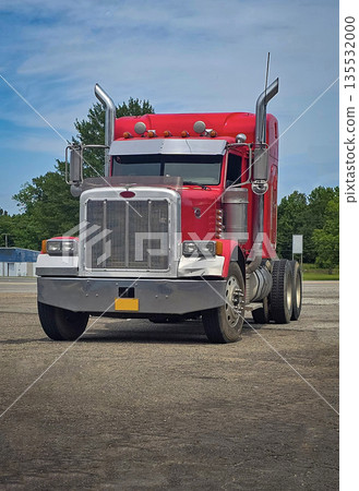 bold red semi truck with a long trailer sits in an open lot during sunset. The powerful rig highlights industrial design, chrome accents, and the rugged appeal of transportation and logistics 135532000