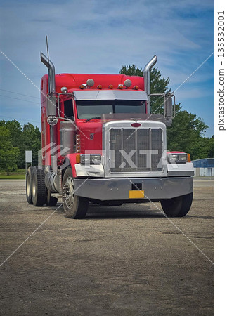 bold red semi truck with a long trailer sits in an open lot during sunset. The powerful rig highlights industrial design, chrome accents, and the rugged appeal of transportation and logistics 135532001