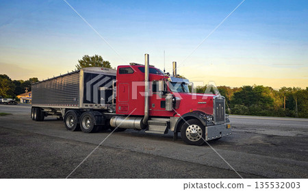 bold red semi truck with a long trailer sits in an open lot during sunset. The powerful rig highlights industrial design, chrome accents, and the rugged appeal of transportation and logistics 135532003