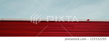 Bright red wall contrasts against cloudy sky in urban setting Bright red wall contrasts against cloudy sky in urban setting 135532293