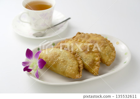 Tea time with three curry fried pies and orchid flowers on a plate on a white background 135532611