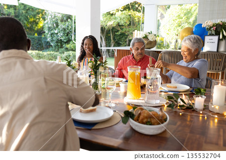 Family enjoying outdoor meal together, sharing laughter and conversation at table Family enjoying outdoor meal together, sharing laughter and conversation at table 135532704