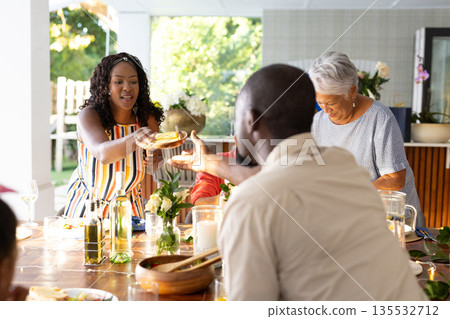 Family enjoying meal together, sharing food and laughter at outdoor dining table Family enjoying meal together, sharing food and laughter at outdoor dining table 135532712