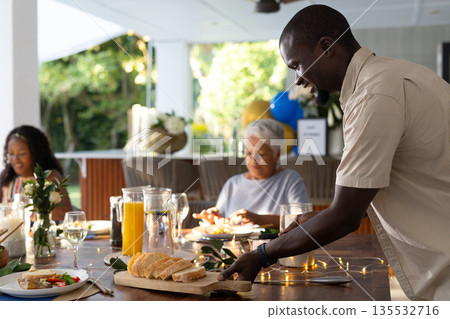 Serving fresh bread at family gathering, smiling and enjoying outdoor meal together Serving fresh bread at family gathering, smiling and enjoying outdoor meal together 135532716