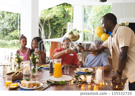 African American man serving drinks at outdoor family meal, everyone smiling African American man serving drinks at outdoor family meal, everyone smiling 135532720