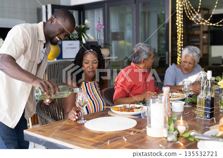 Outdoor family meal, man pouring wine while everyone smiling and talking together 135532721